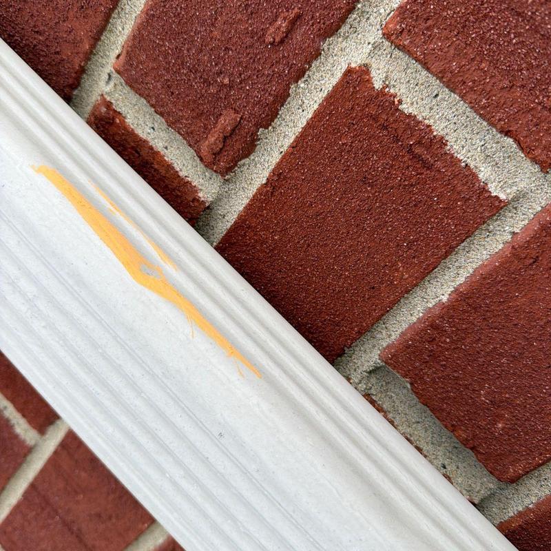 Gutter with yellow paint mark on brick wall background