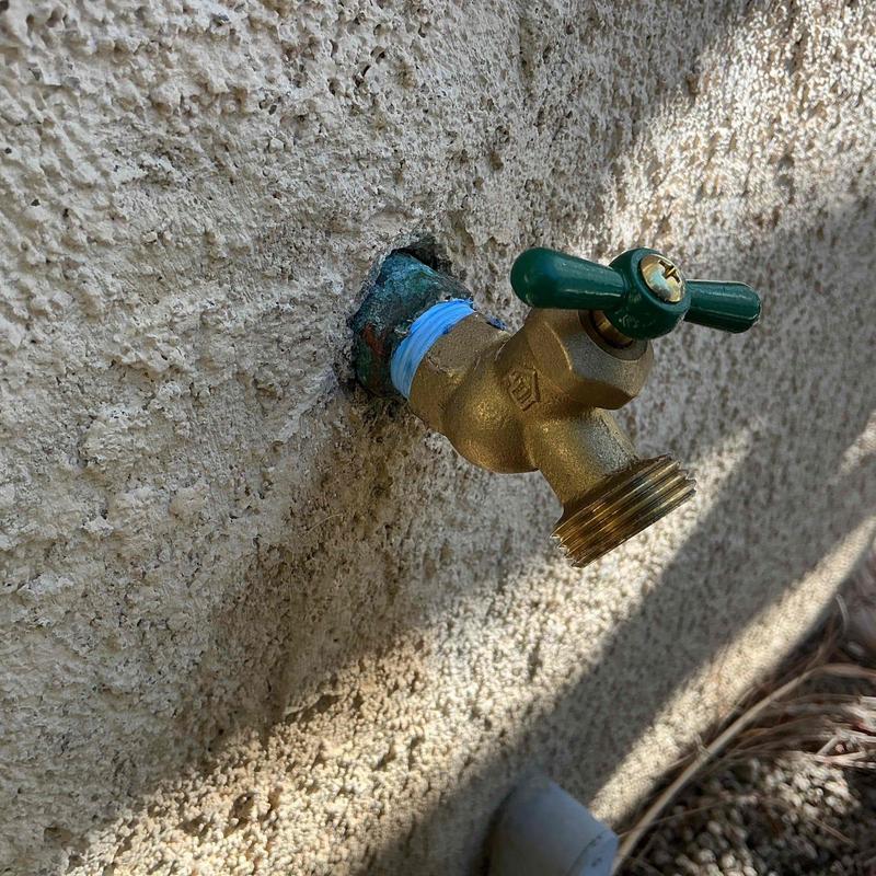 No-kink hose bib with green handle on stucco wall
