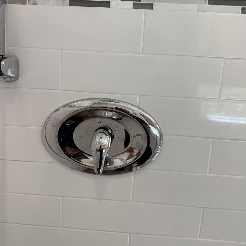 Shower valve with chrome handle on white tile wall