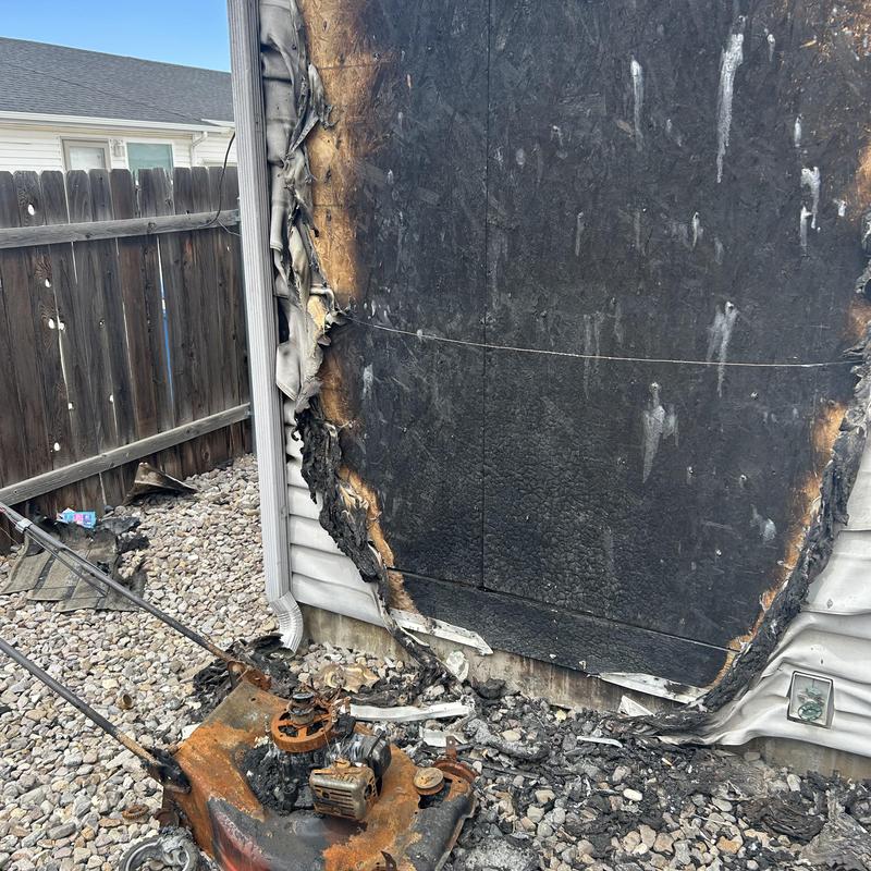 Burned exterior siding with fire-damaged lawn mower Burned exterior siding with fire-damaged lawn mower