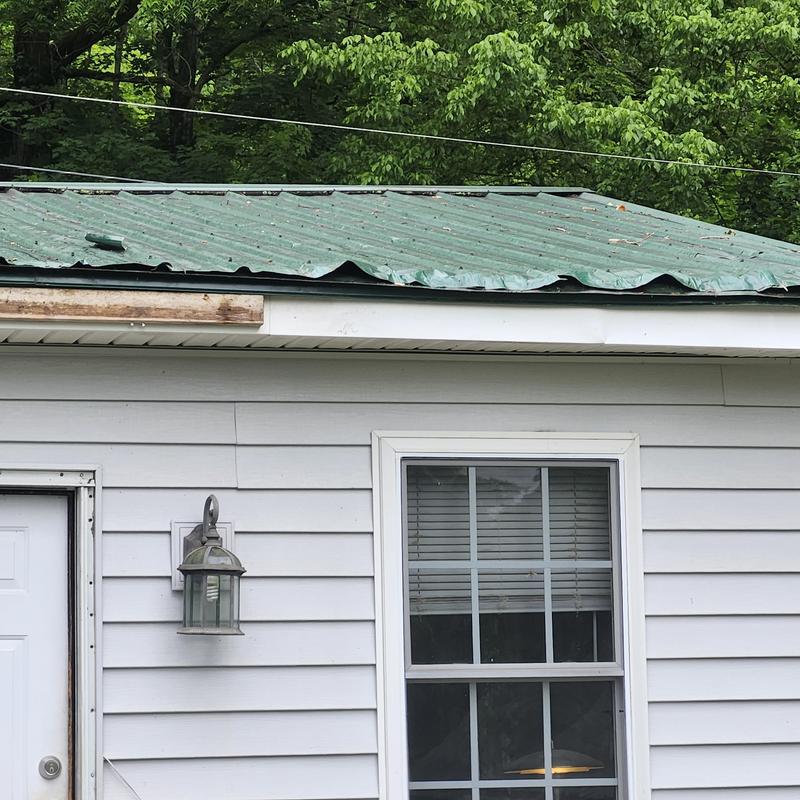 Metal roof damage from fallen tree limb above door and window