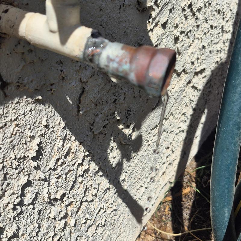 Outdoor hose bib with dripping water on stucco wall