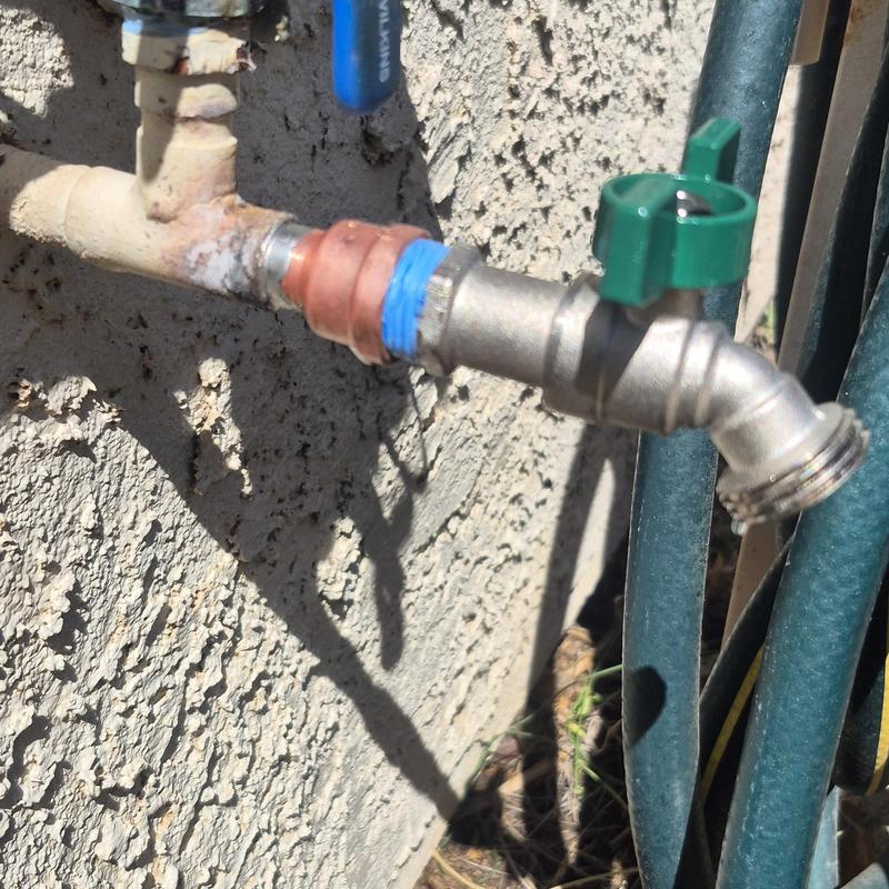 Outdoor hose bib with green handle and hose attached