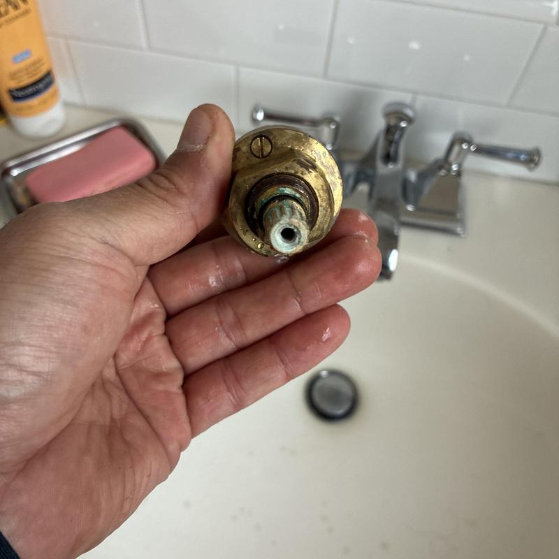 Shower faucet cartridge held by hand over sink basin