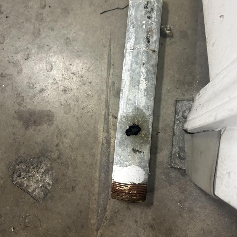 Galvanized pipe with corrosion hole on concrete floor Galvanized pipe with corrosion hole on concrete floor