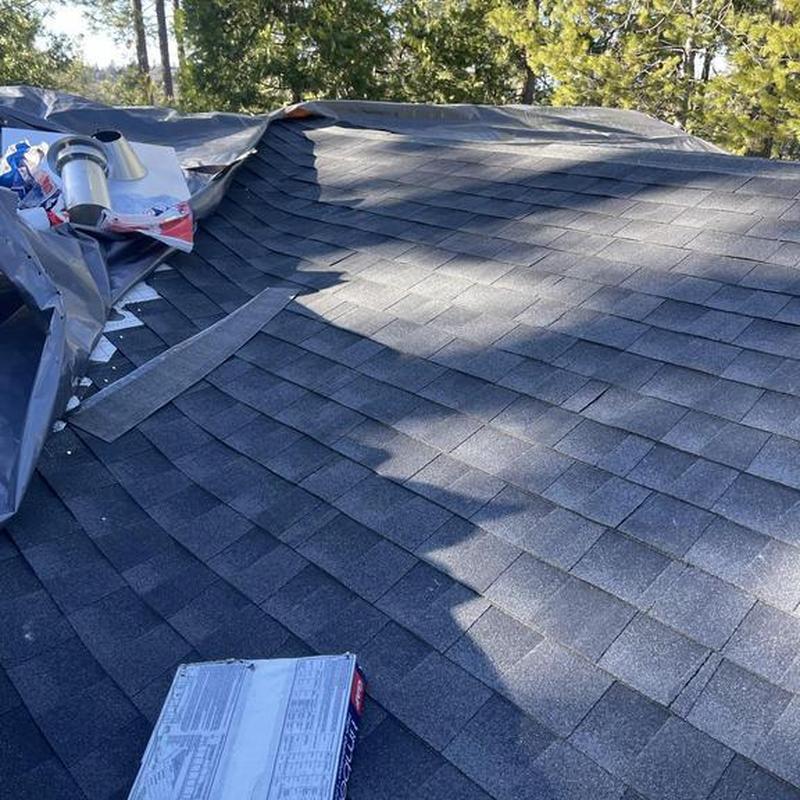Asphalt shingle roof installation with vent pipe in trees