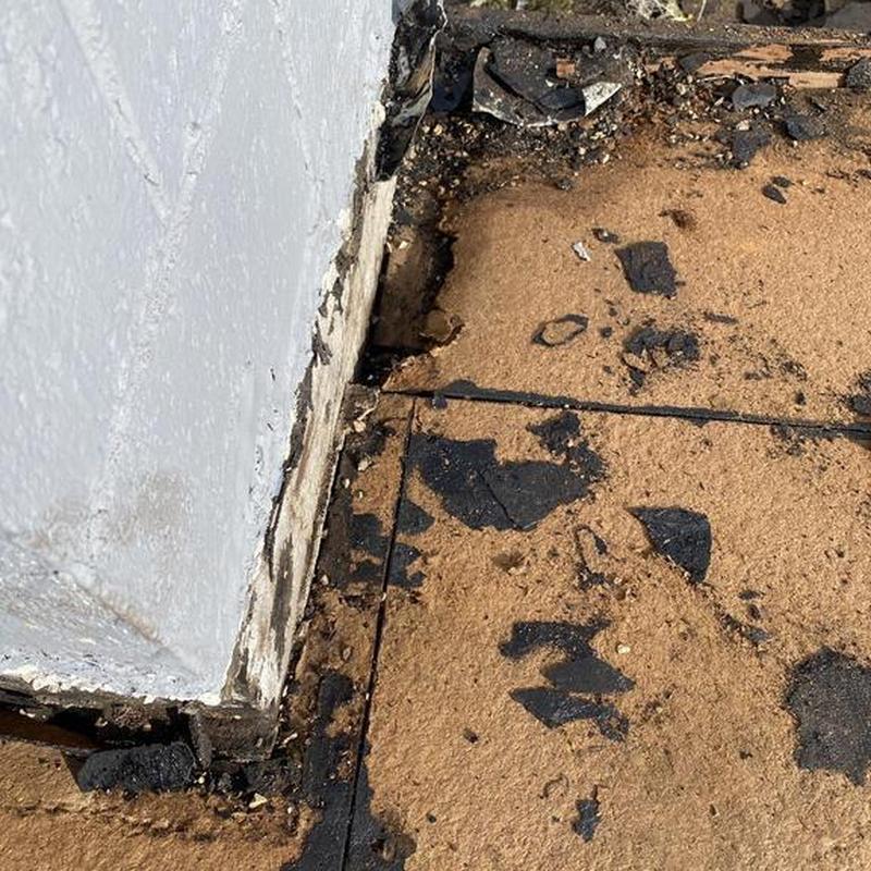 Torch down roofing material with damaged edges near wall base