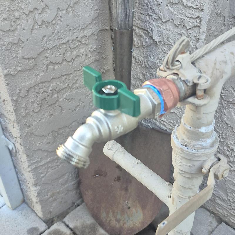 Outdoor hose bib with green handle on wall piping