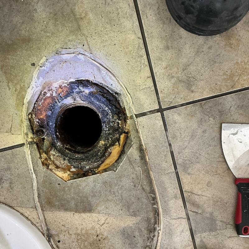 Toilet flange with old wax ring residue on tiled floor