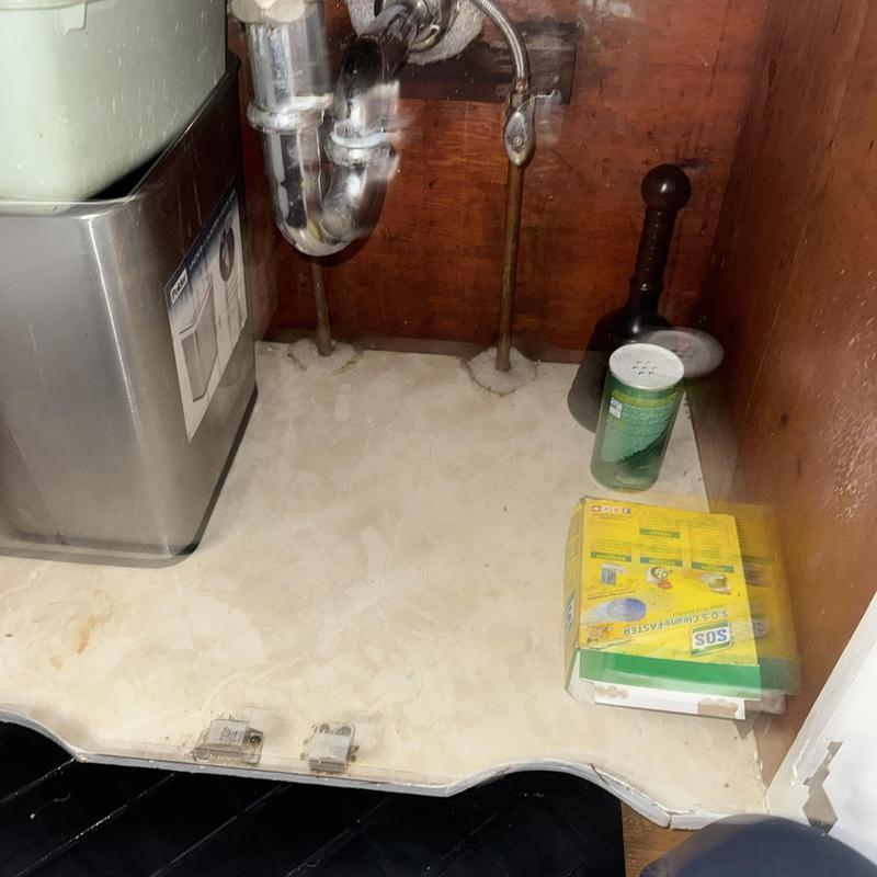 Kitchen sink drain with plumbing tools and cleaner inside cabinet