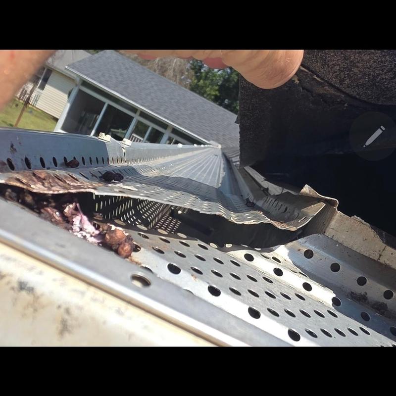 Metal gutter guard with debris damage near roof edge