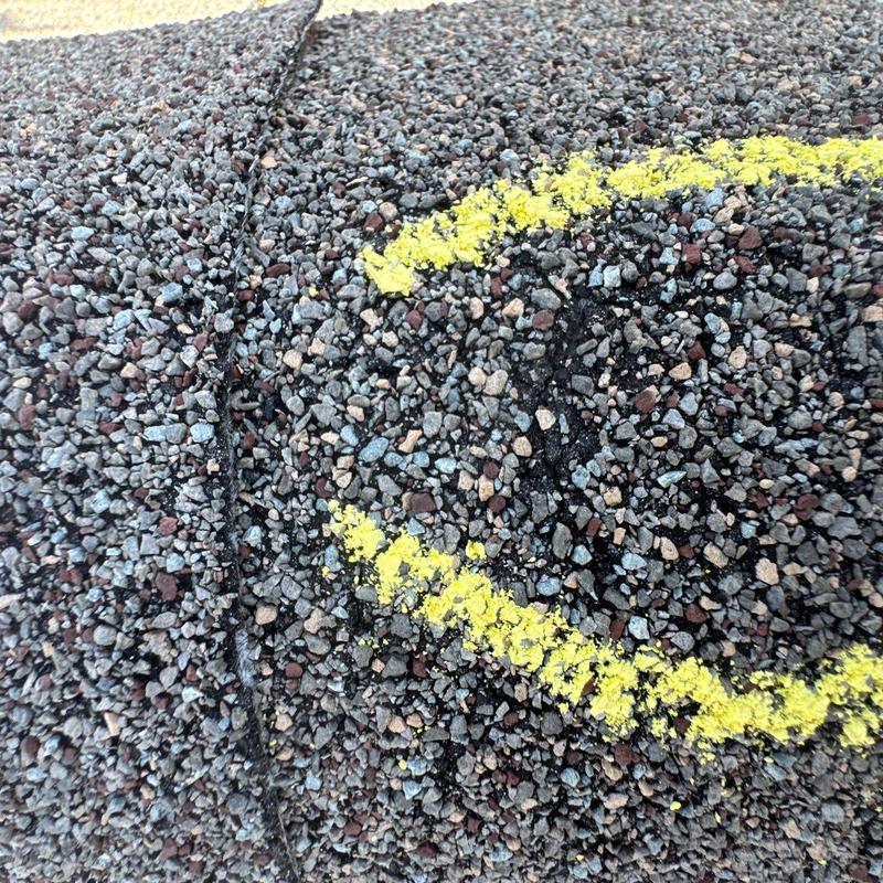 Asphalt roofing shingle with hail damage marked in yellow