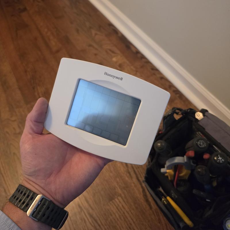Honeywell thermostat held over hardwood floor near tool bag
