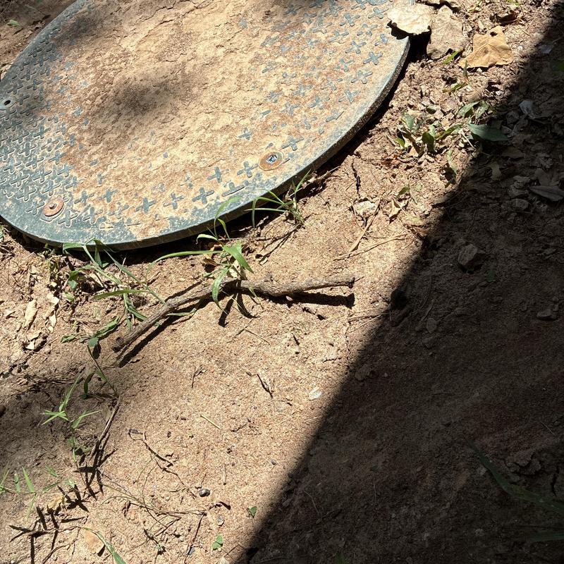 Sewer cleanout cover in dry dirt with grass and shadow Sewer cleanout cover in dry dirt with grass and shadow
