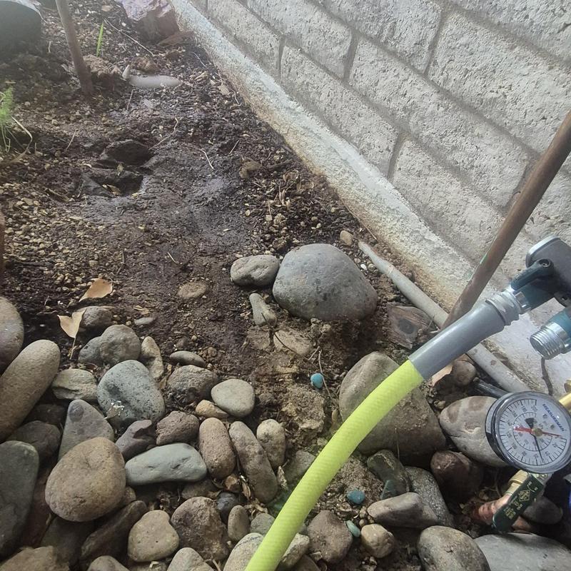 Water pressure gauge and hose near stone and soil bed