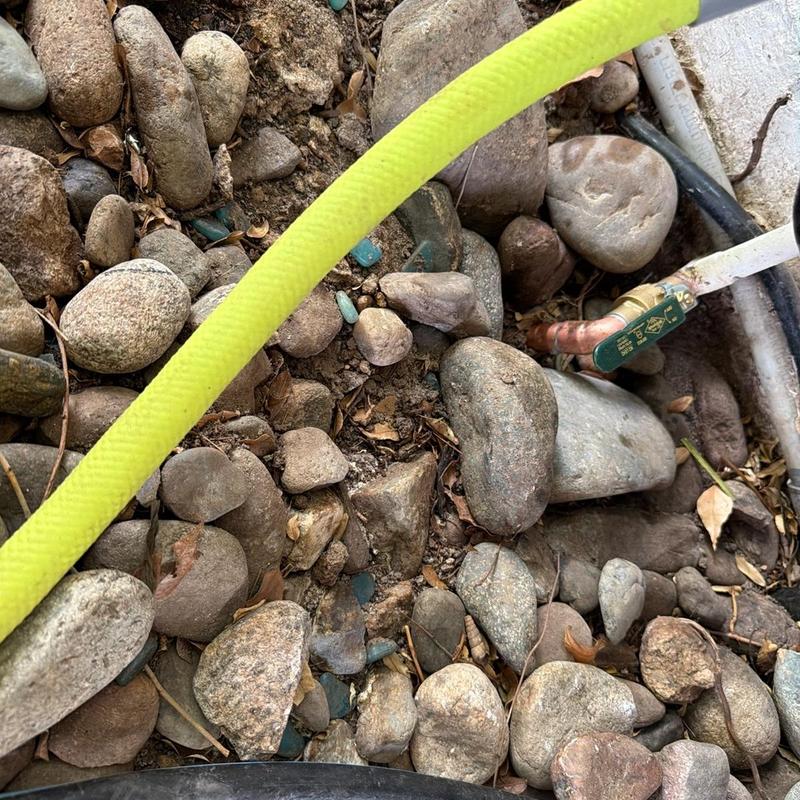 Outdoor gas line valve and yellow hose among rocks