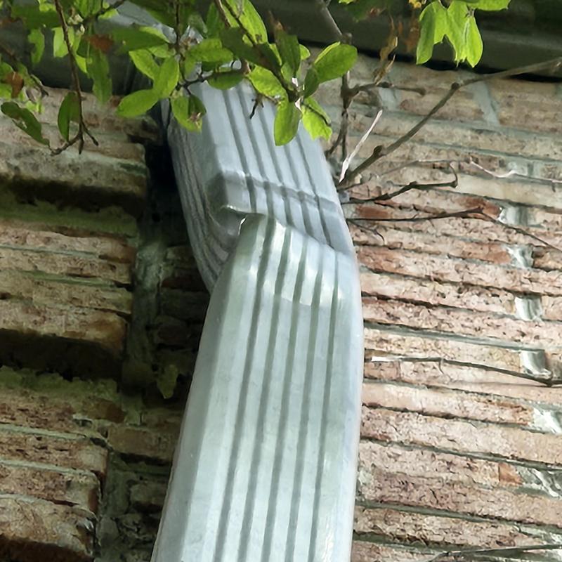 Metal gutter downspout bent and detached from brick wall