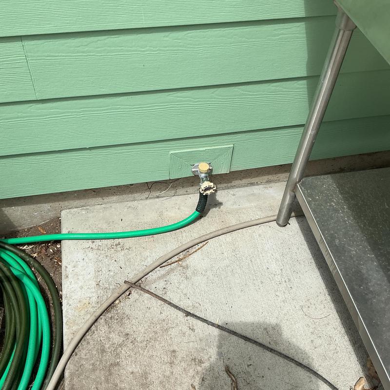 Outdoor hose bibb with attached green garden hose on green siding