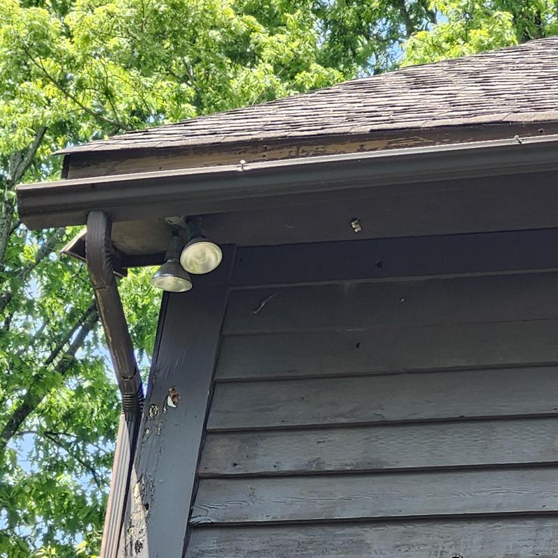 Gutter and downspout on dark wood siding under roof edge