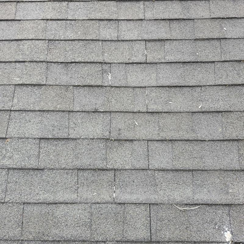Gray asphalt roof shingles close-up with minor damage