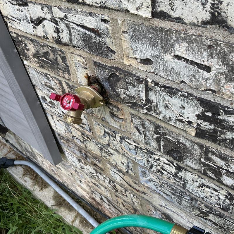 Hose bib with red handle installed on brick wall Hose bib with red handle installed on brick wall