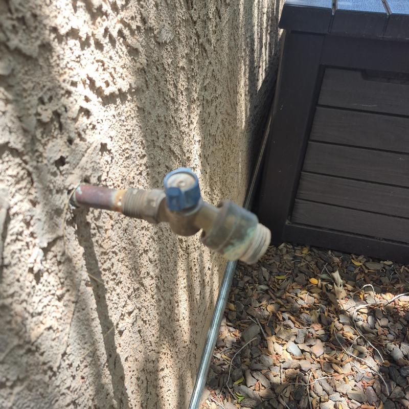 Outdoor hose bib with blue handle on stucco wall