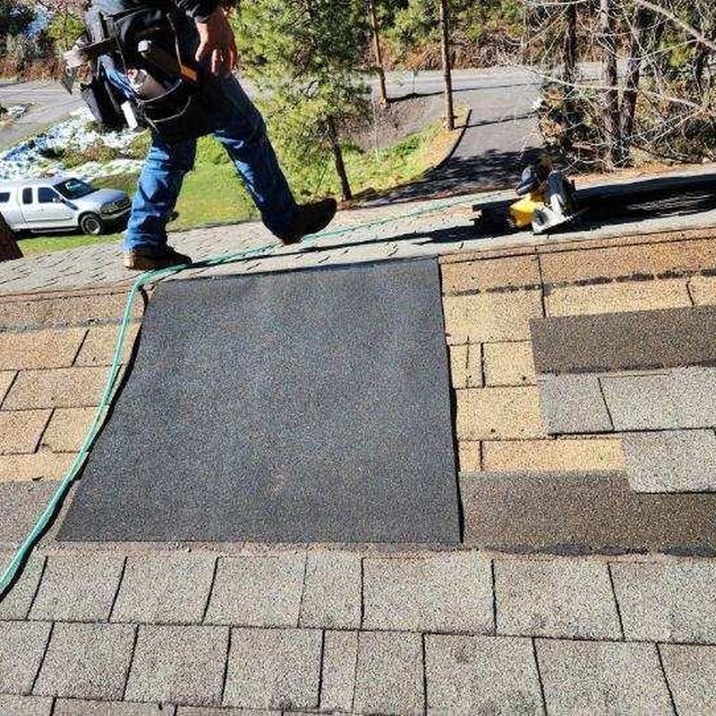 Asphalt shingle roof patch with worker on roof