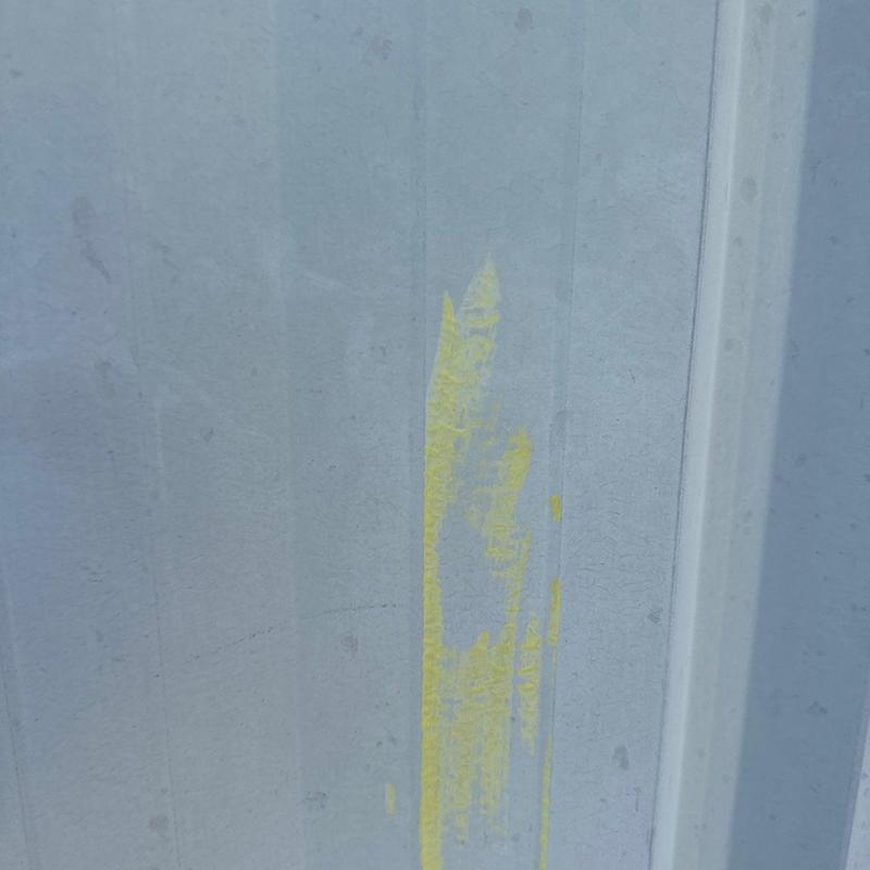 Metal roof panel with yellow paint mark and hail damage