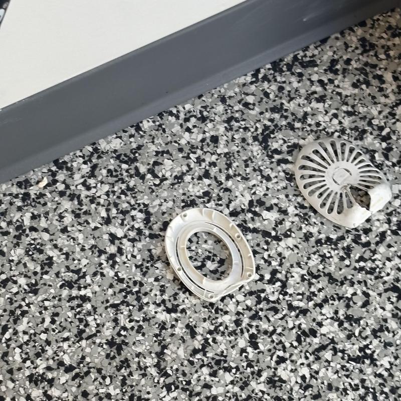Toilet flange and broken plastic cover on speckled floor Toilet flange and broken plastic cover on speckled floor