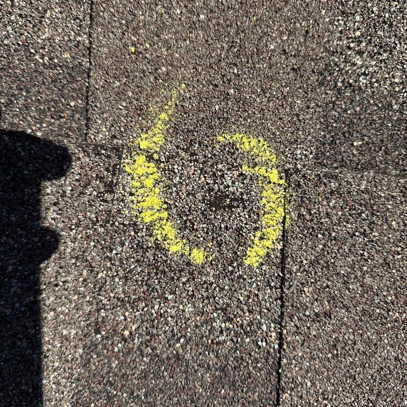 Roof shingles with yellow chalk marking damaged spot