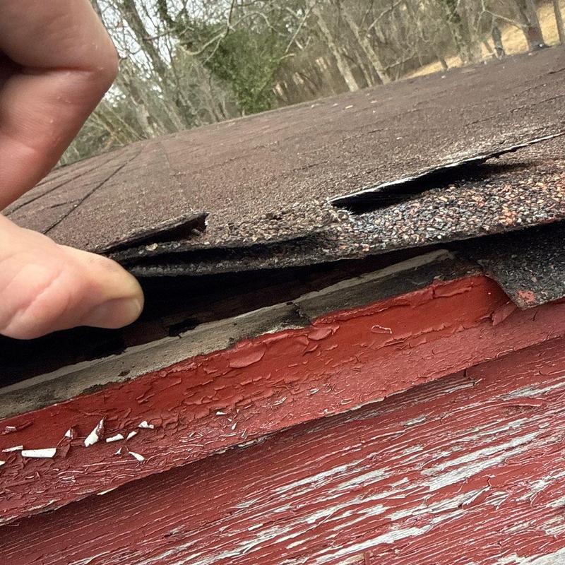 Roof shingles lifted revealing wood damage beneath