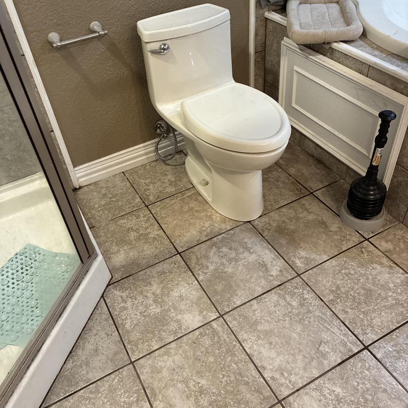 Toilet in bathroom with plunger on tile floor Toilet in bathroom with plunger on tile floor