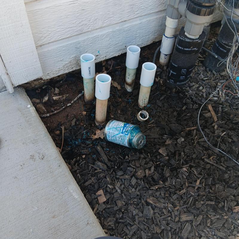 Sprinkler valve pipes near exterior wall with soil mulch