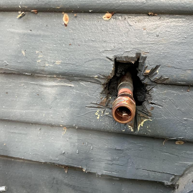 Hose bib copper pipe protruding from wall siding hole Hose bib copper pipe protruding from wall siding hole