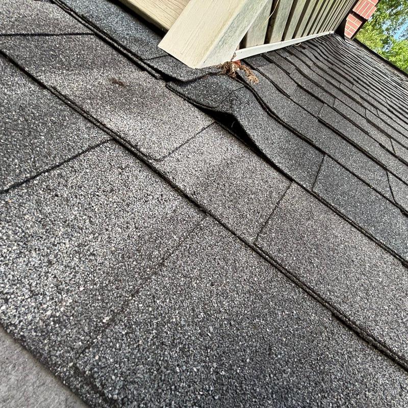 Asphalt shingle roof with lifted shingles near wall transition