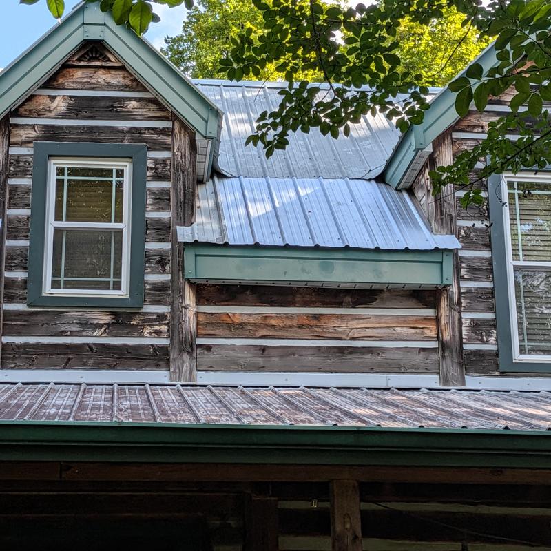 Metal roof panels on log cabin house under trees
