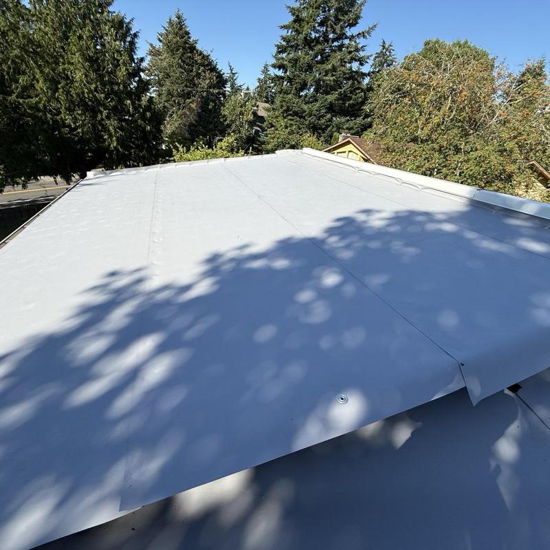Flat rubber membrane roofing installation with tree shadows