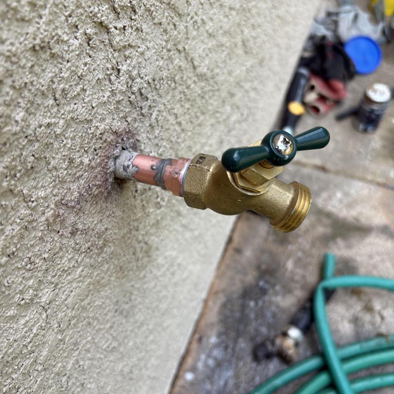 Hose bib valve installed on exterior wall with hose attached Hose bib valve installed on exterior wall with hose attached