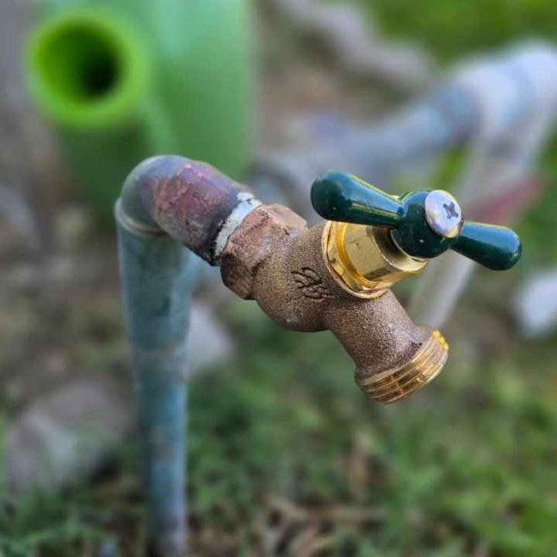 Soldered hose bib with green handle on outdoor pipe