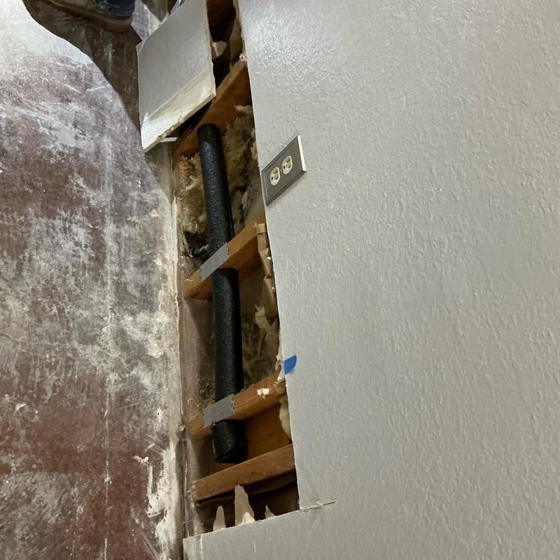 Insulated black PEX line in wall cavity near outlet