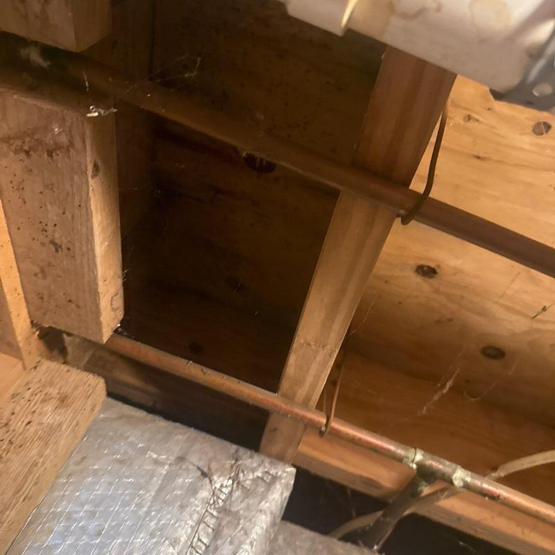 Copper plumbing pipes under attic wooden beams and insulation