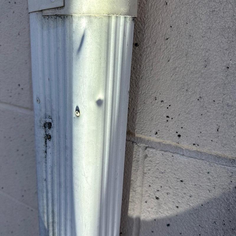 Downspout with hail damage on commercial roof wall