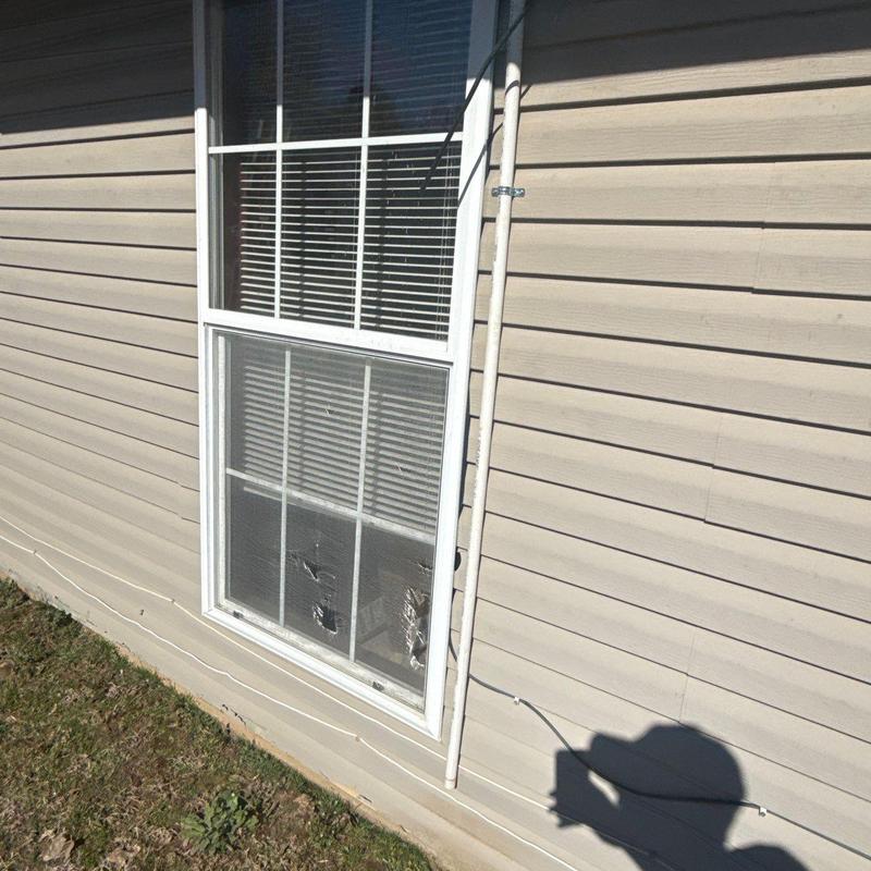 Window glass with visible cracks in residential siding wall