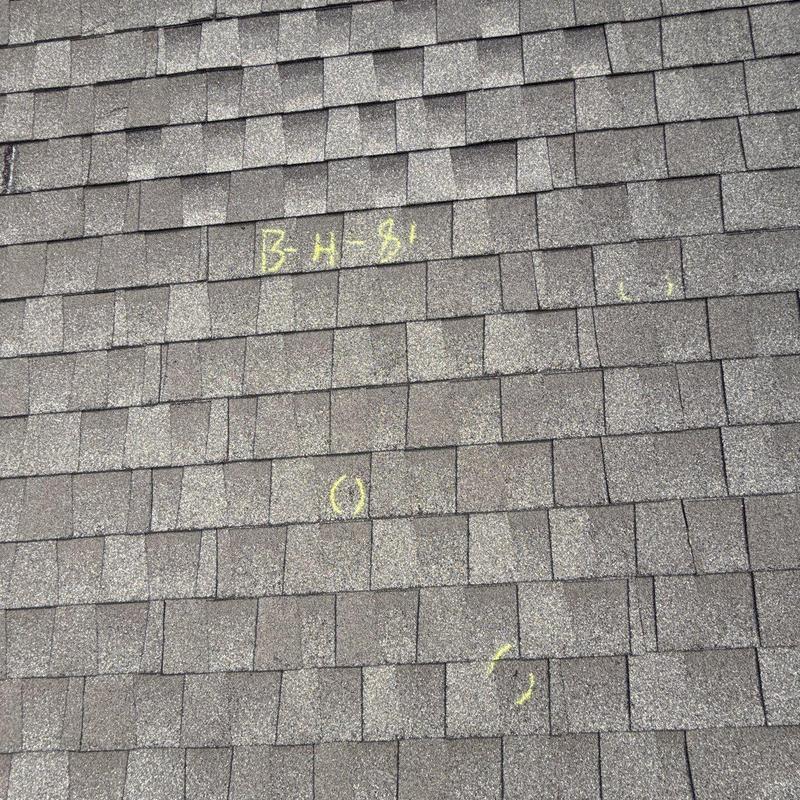 Asphalt roof shingles with hail damage marked in yellow chalk