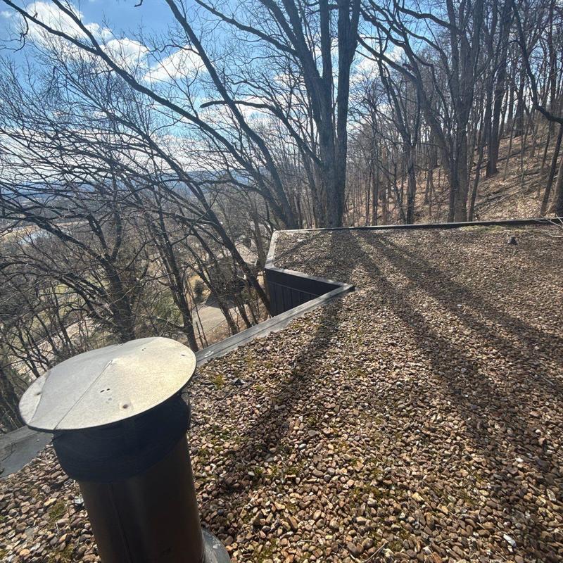 Gravel flat roof with metal vent pipe and trees