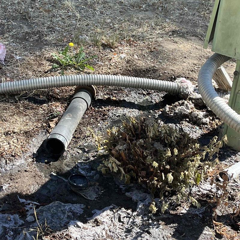 Open sewer pipe with drainage hose on dry ground