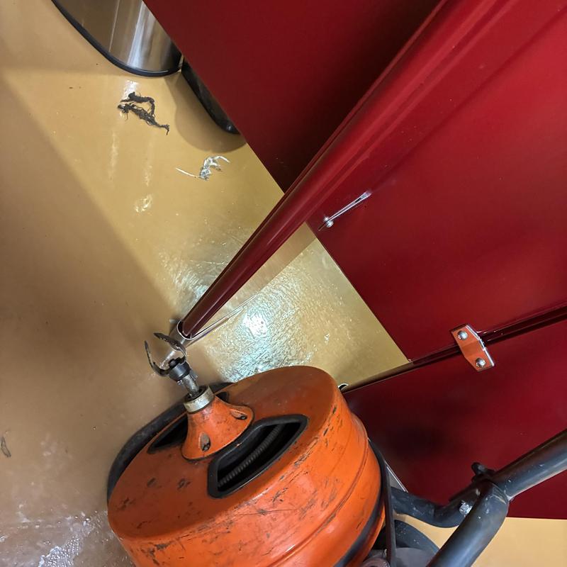 Men's restroom drain snaking tool by red stall door Men's restroom drain snaking tool by red stall door