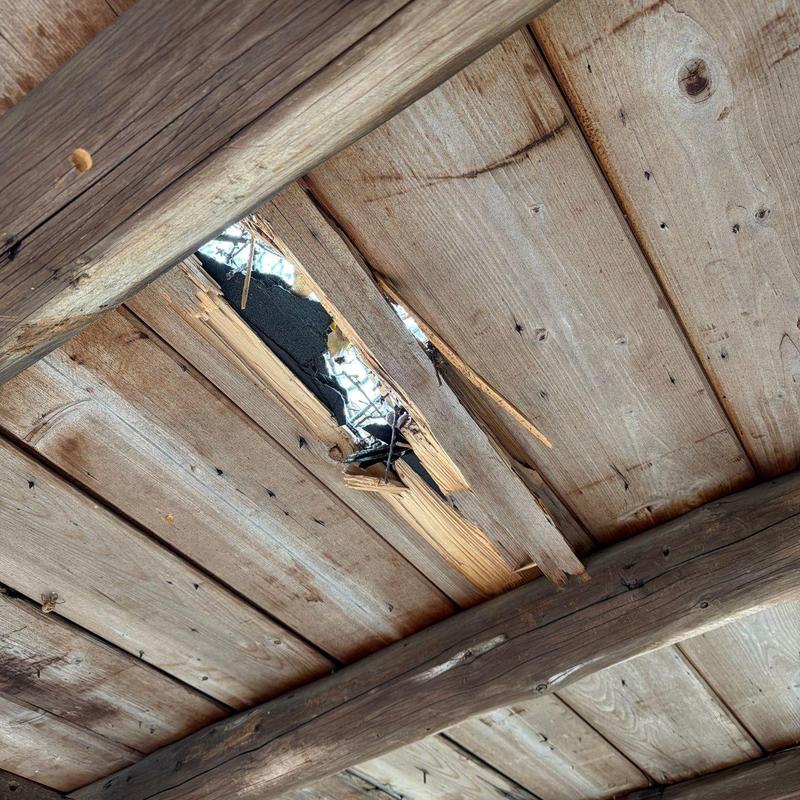 Wood roof decking with large hole and damage visible