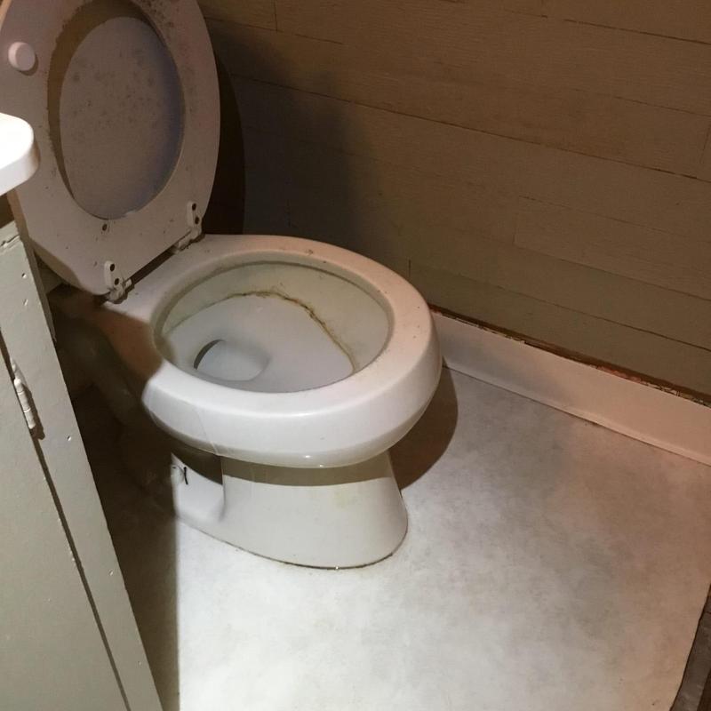 Toilet bowl with stains and open lid in bathroom corner