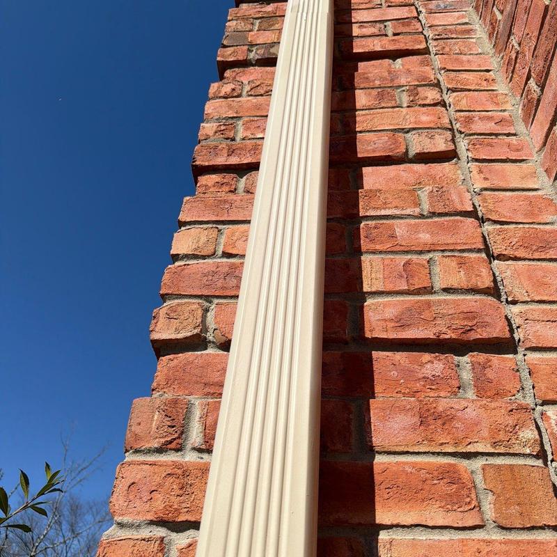 Vinyl downspout attached to red brick wall outdoors